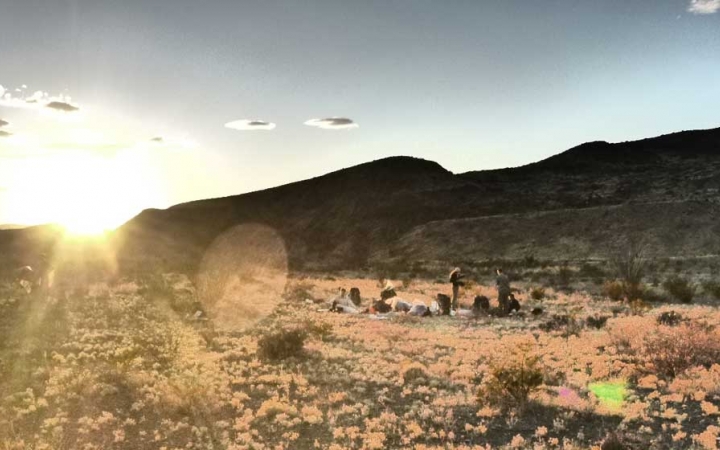 the campsite of a group of outward bound backpacking students sits in a desert landscape as the sun sets behind a ridge in the background